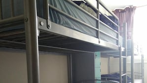 Une chambre avec un lit superposé doté de barrières métalliques et un lit simple recouvert d’une couverture bleue.