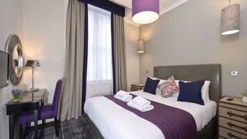 A hotel room with a large bed, a desk with a chair, a mirror, and a window with curtains.