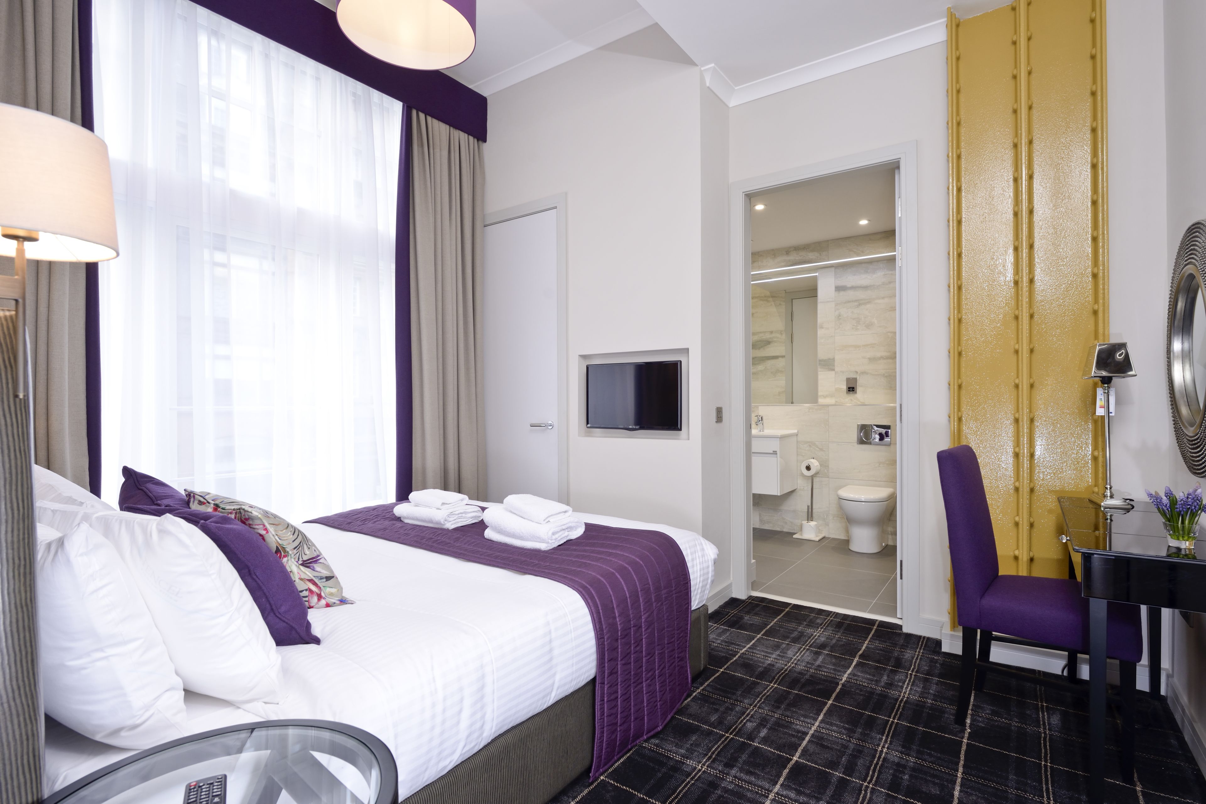 A hotel room with a bed, a television, a bathroom with a toilet and sink, and a chair.