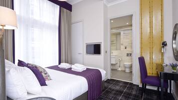 A hotel room with a bed, a television, a bathroom with a toilet and sink, and a chair.