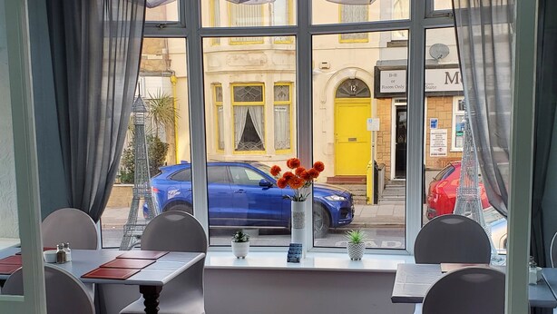 En restaurant med rød løber, hvide stole og et bord med en blomstervase.