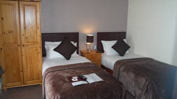 Een hotelkamer met twee bedden, een houten kledingkast, een nachtkastje met een lamp en een afstandsbediening op de bedden.