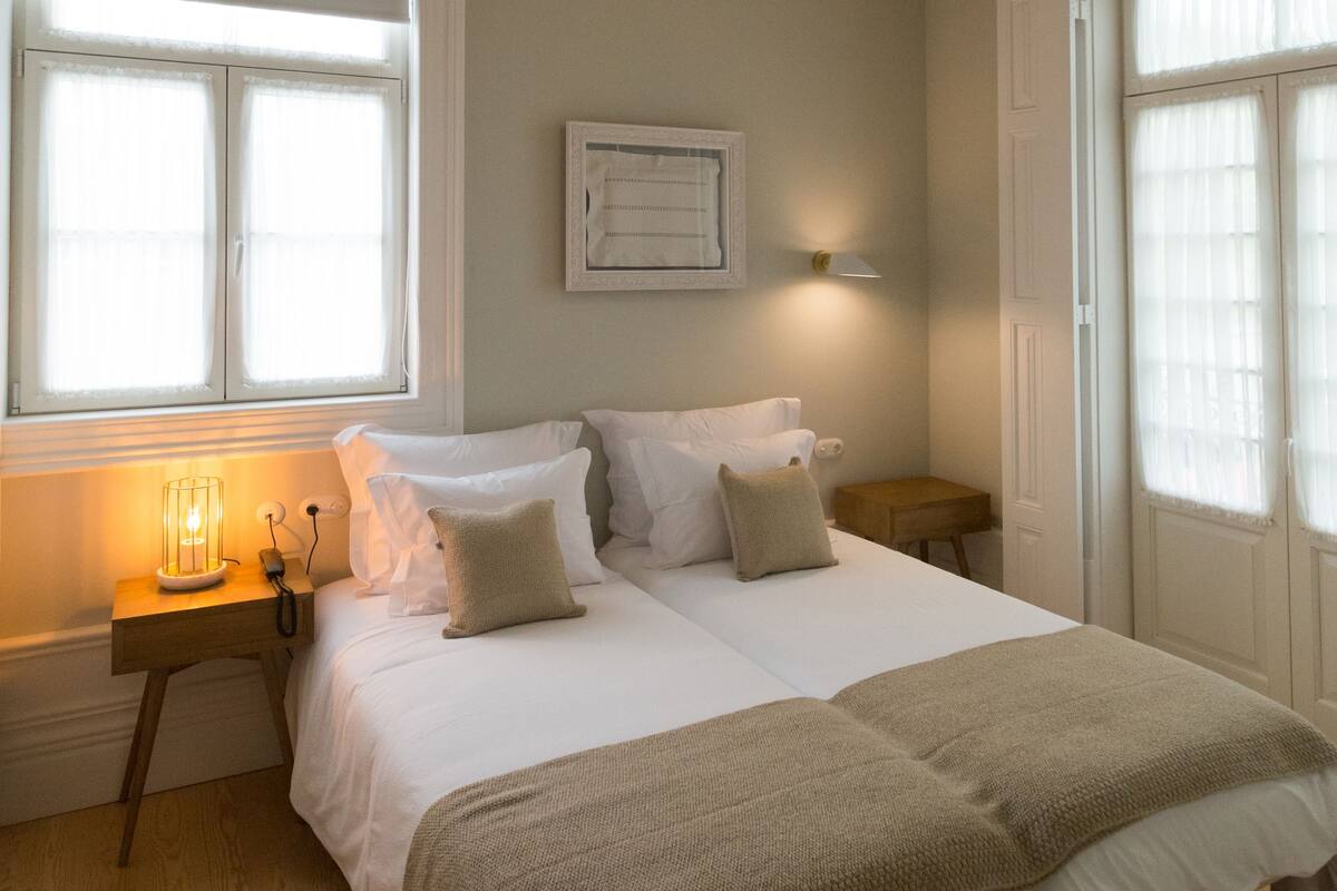 A bedroom with a bed, bedside tables, a hanging light fixture, and a window with blinds.