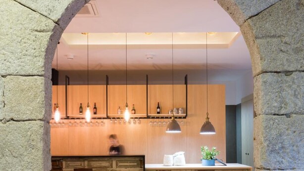 Una cocina moderna con piso a cuadros, arco de piedra, armarios de madera e iluminación colgante.