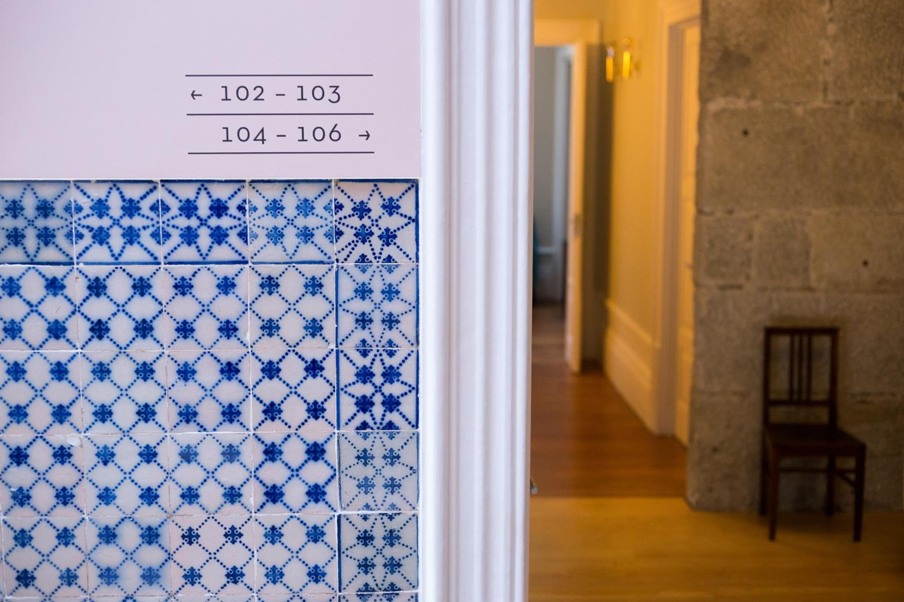 Un couloir avec un mur recouvert de carreaux présentant des motifs géométriques et une chaise.
