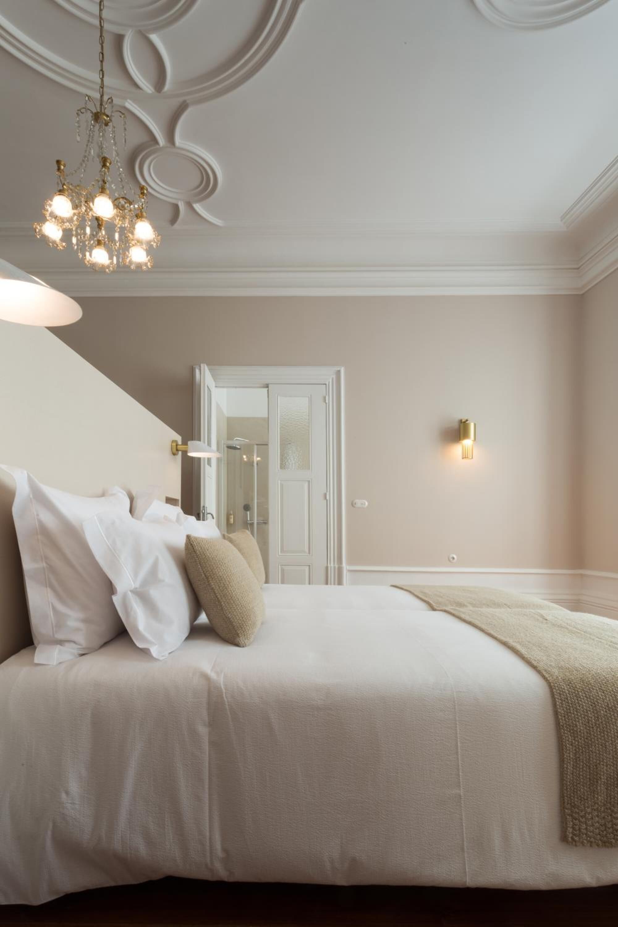 Une chambre à coucher avec un grand lit, un lustre, une applique murale et une porte donnant sur une salle de bain.