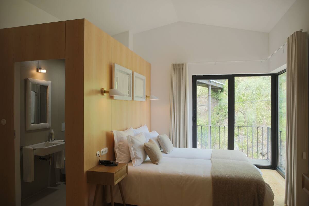 A modern hotel room with a large bed, a bathroom, and a balcony with a view.