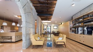 Un moderno vestíbulo de hotel con una columna de piedra, suelo de madera, una recepción, sofás, un soporte para vinos y un comedor.