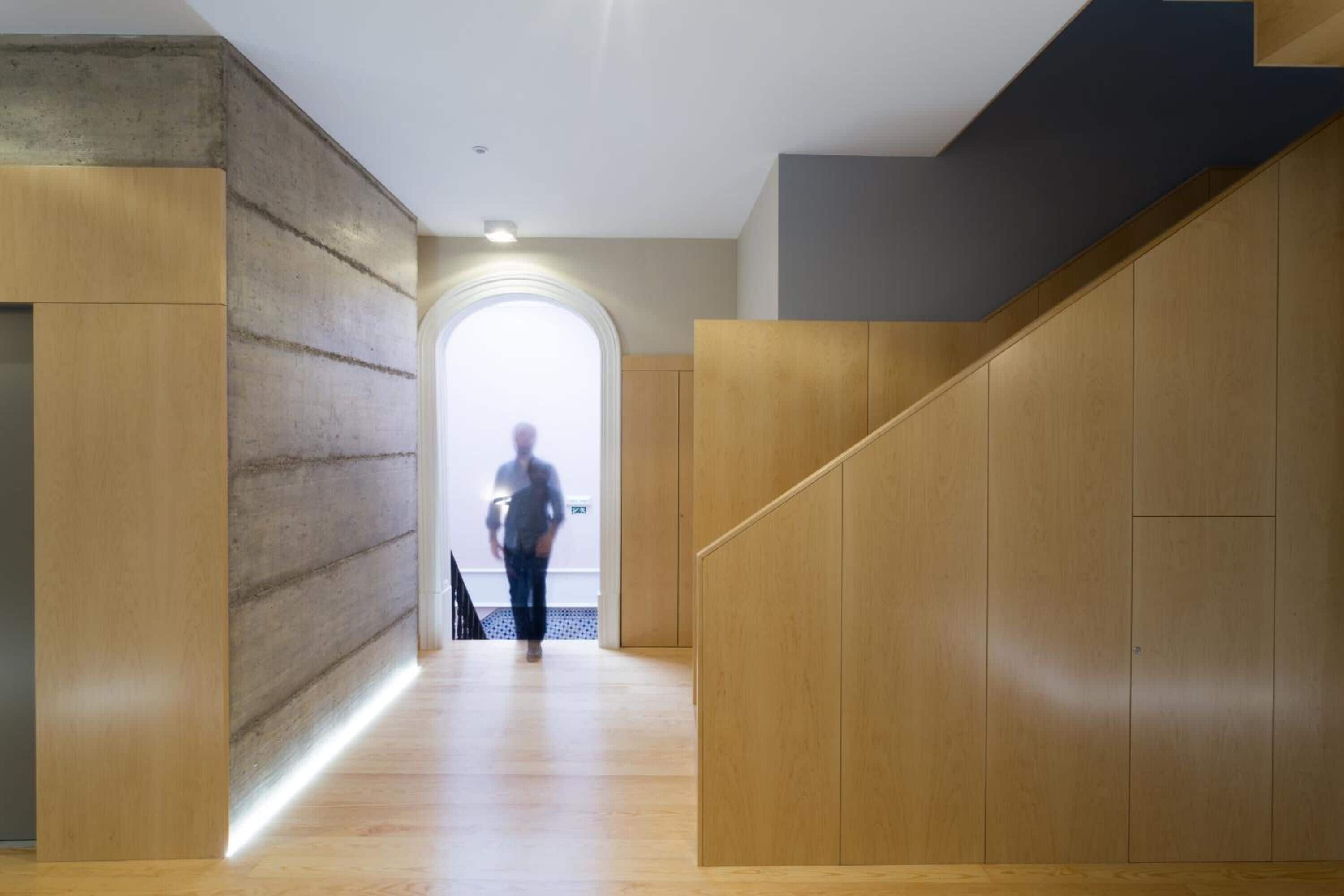 A modern interior with a wooden floor, a concrete wall, and a wooden staircase.