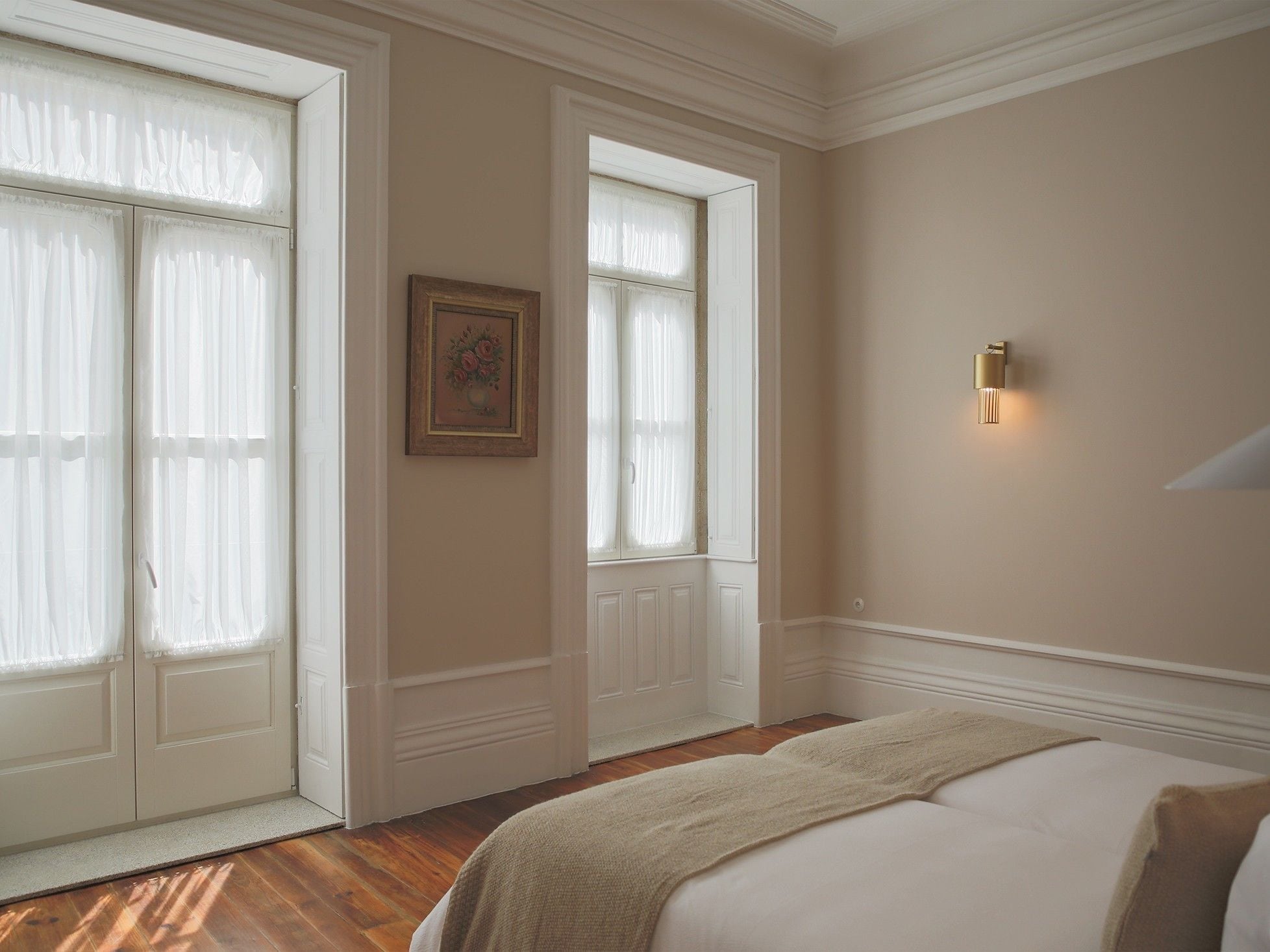 A hotel room with a large bed, a door with a white frame, and a wall-mounted light fixture.