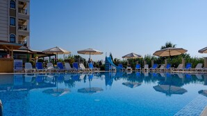 Una piscina con azulejos azules, sillas de descanso y sombrillas.