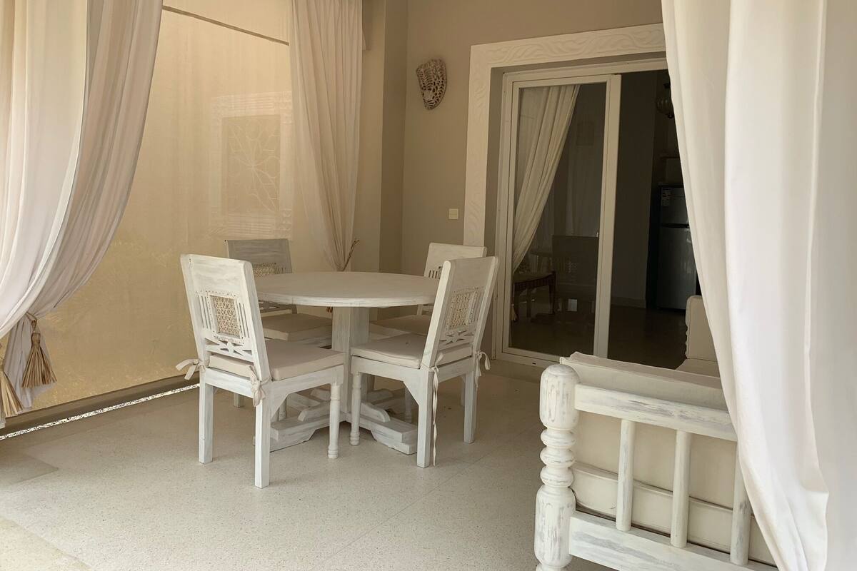 A dining area with a round table and four chairs, a sliding glass door, and a light fixture.