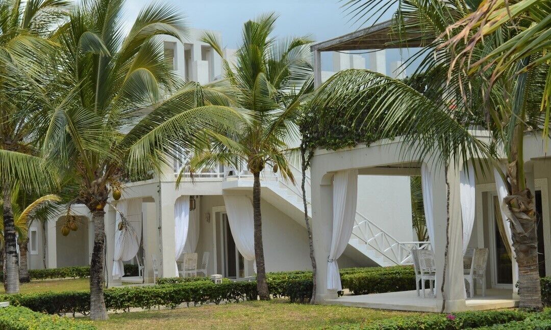 Un resort con edificios blancos, palmeras y una zona de estar techada al aire libre.
