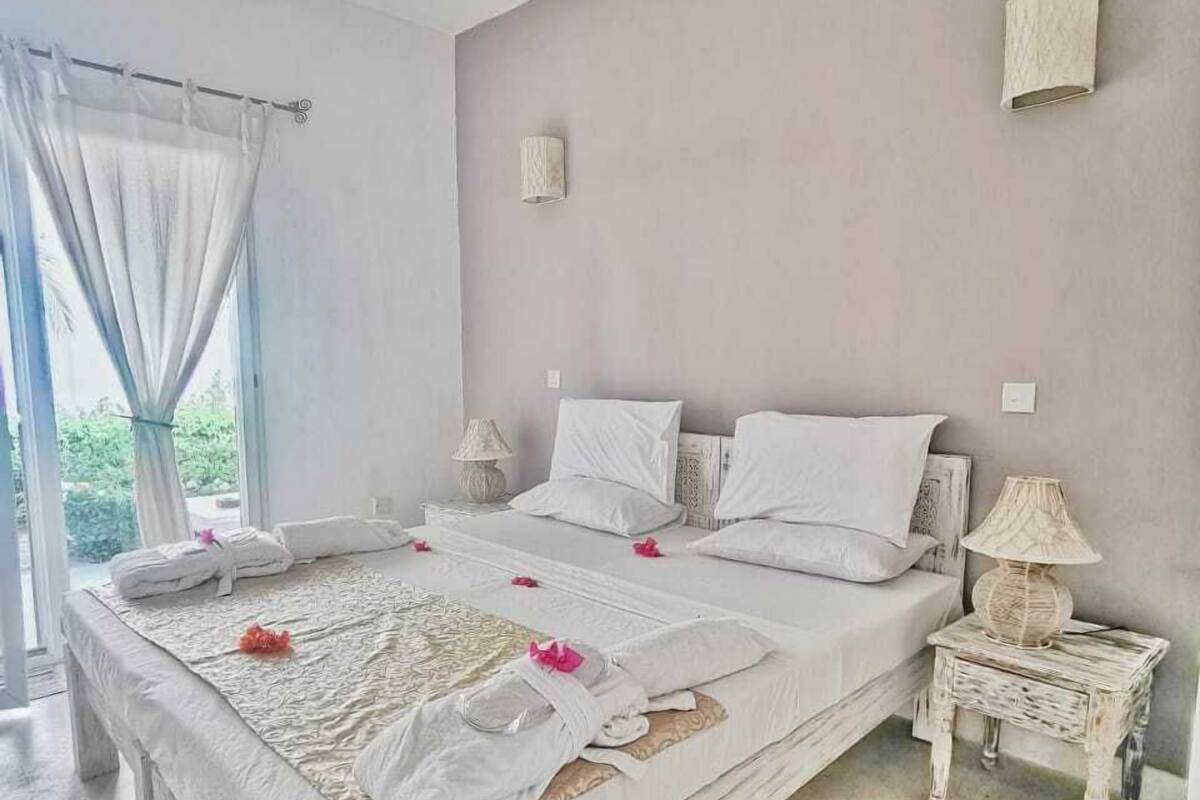 A spacious bedroom with a large bed, two bedside tables, and a view of greenery outside.