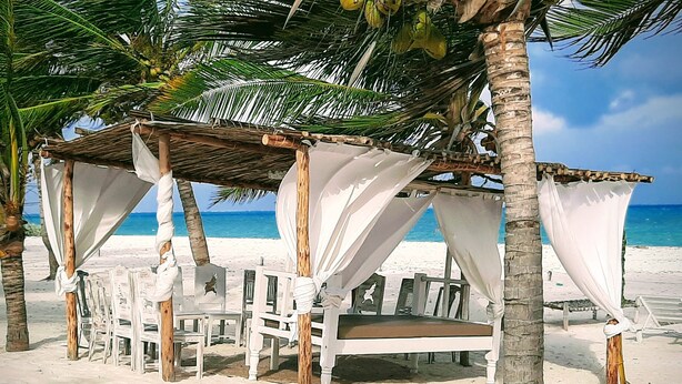 A beach cabana with white chairs and a thatched roof, overlooking the ocean. - Life Resort St.Thomas Royal Palm (Watamu)