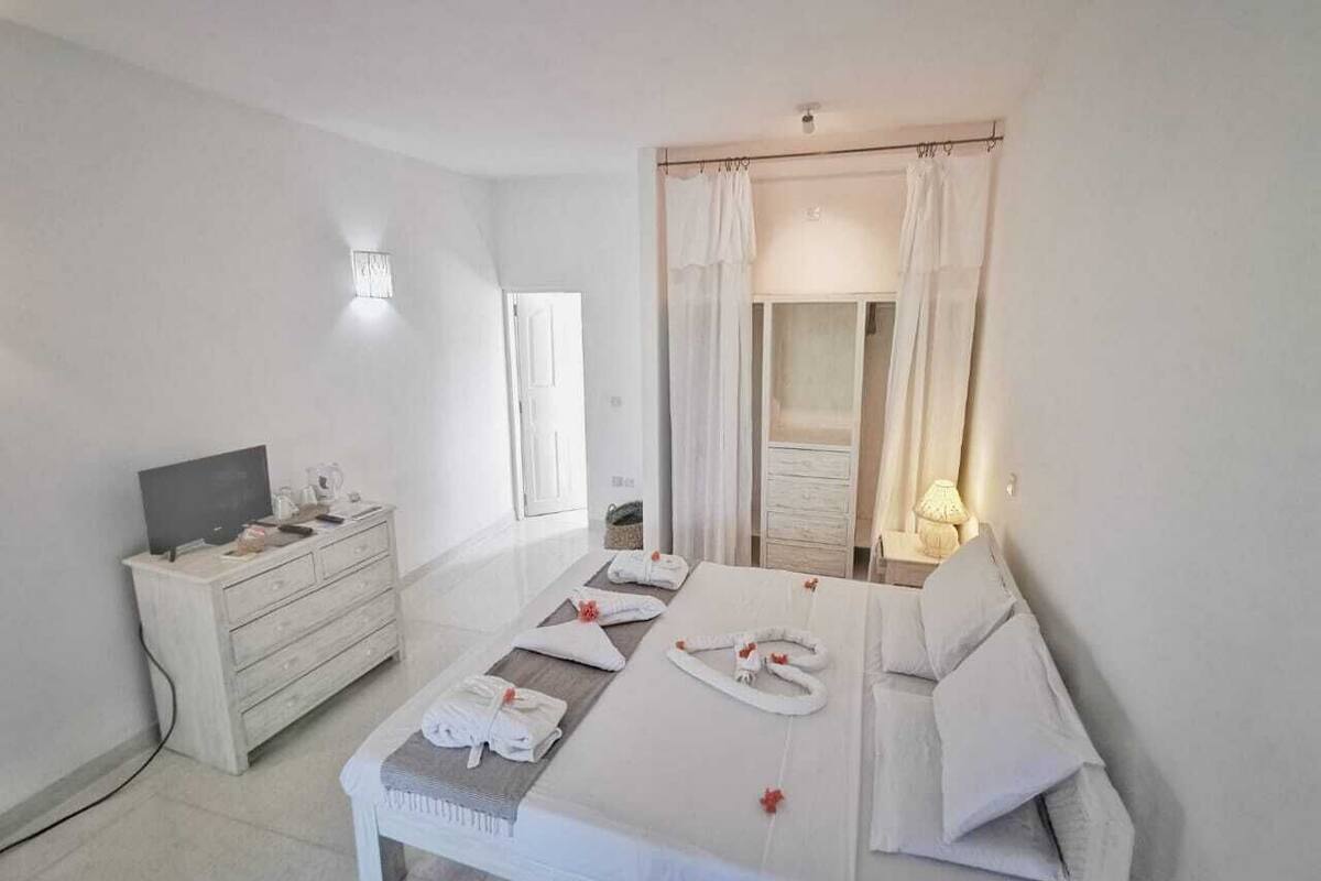 A hotel room with a bed, a TV, a dresser, and a window with curtains.