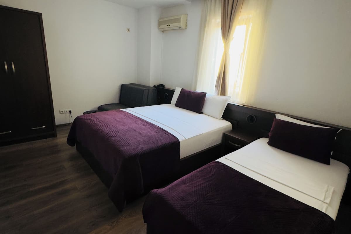 A hotel room with two single beds, a wardrobe, a desk, and a window with curtains.