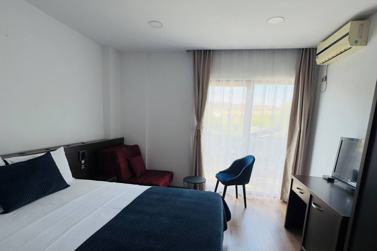 A hotel room with a large bed, a desk, a chair, and a TV.