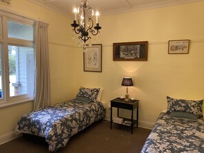 Een slaapkamer met twee bedden, een kroonluchter, een klein tafeltje met een lamp en ingekaderde foto’s aan de muur.