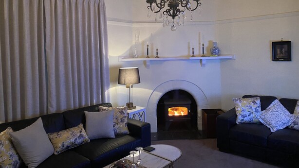 A living room with a fireplace, two sofas, a chandelier, and a table with a lamp. - On the banks of the Huon River, in the heart of HuonValley (Huonville)