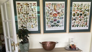 A room with a wooden console table, a copper bowl, a potted plant, a vase with flowers, and framed botanical illustrations on the wall. - On the banks of the Huon River, in the heart of HuonValley (Huonville)