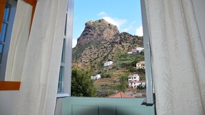 Vista des d'una finestra amb cortines, amb una muntanya i edificis al fons.