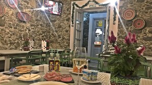 Taula de menjador preparada amb plats, coberts i menjar, amb un televisor que mostra una escena nadalenca al fons.