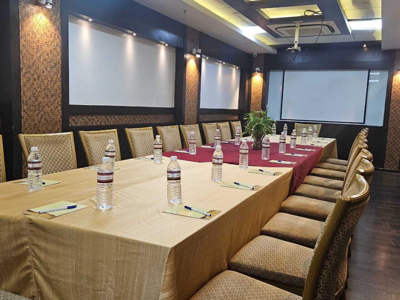 Un salón de conferencias con una larga mesa, sillas, botellas de agua y una pantalla de proyector.