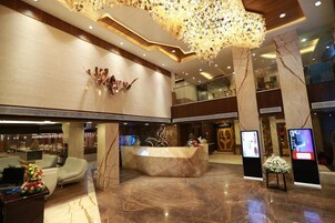 A hotel lobby with a reception desk, seating area, and a decorative ceiling light fixture.