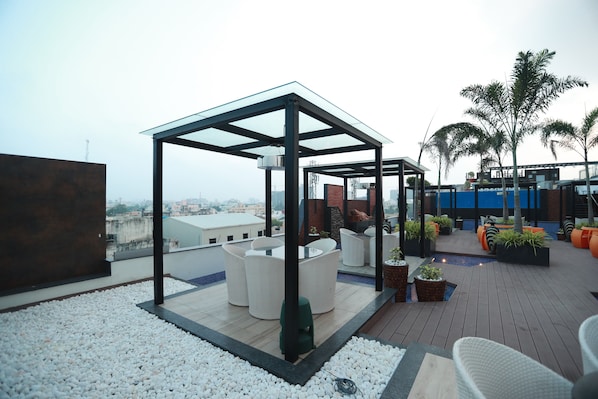 Una terraza en la azotea con un pabellón de cristal, mobiliario exterior y plantas en macetas.