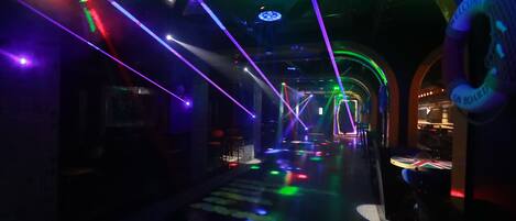 Um corredor mal iluminado com luzes laser coloridas e um letreiro circular com o texto 'WELCOME ON BOARD'.