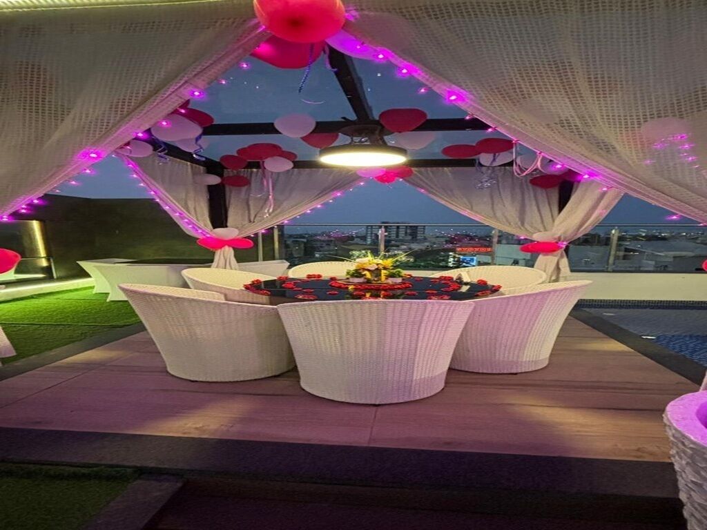 Un espacio al aire libre con mobiliario de mimbre blanco, un arreglo floral e iluminación decorativa.