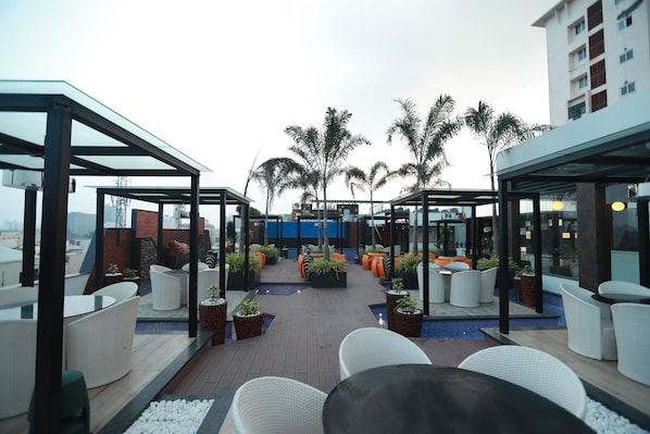 Terraza en la azotea con mobiliario exterior, palmeras y vistas de la ciudad.