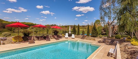 A swimming pool with red umbrellas, lounge chairs, and a view of the surrounding landscape.