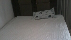 Un lit avec un matelas matelassé blanc et un oreiller orné d’un motif géométrique.