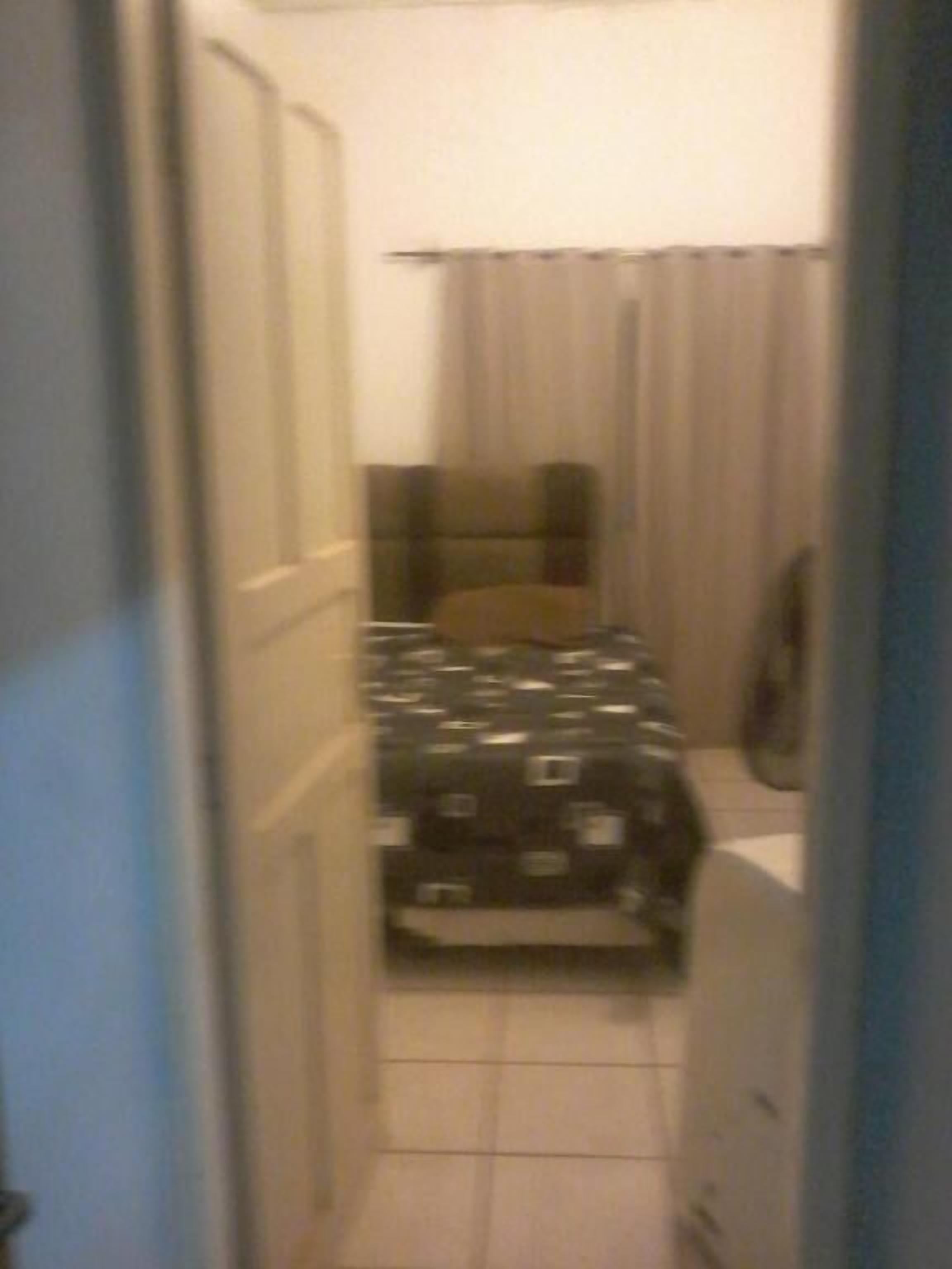 Un estrecho pasillo que conduce a un dormitorio con una cama, un armario y un espejo.