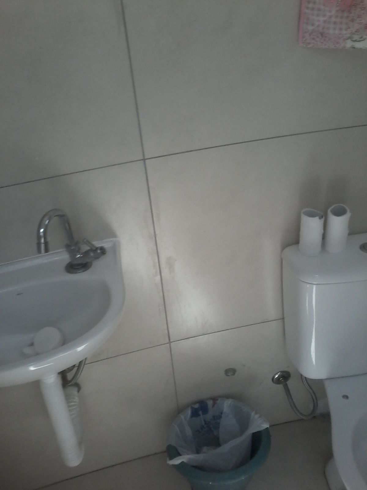 A bathroom with a sink, toilet, and trash bin.