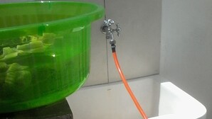 Une salle de bain avec un lavabo vert, un évier blanc et un tuyau d’eau orange.