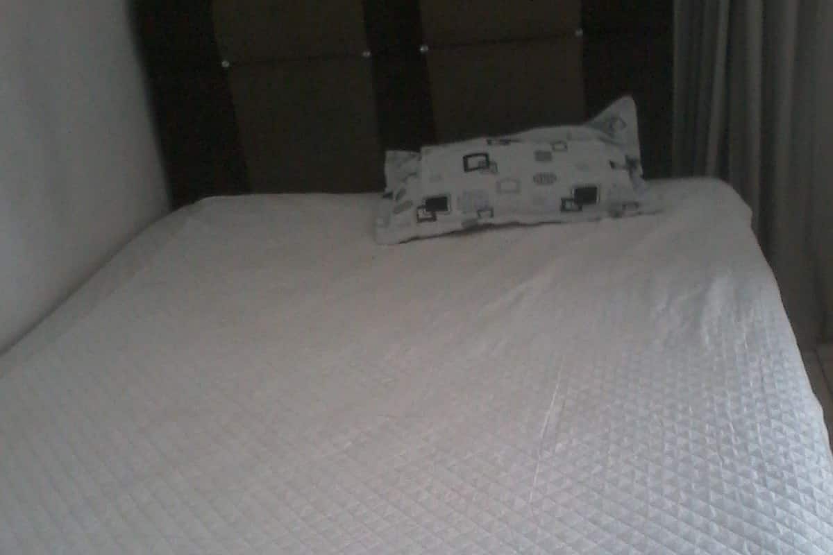 Una cama con colchón acolchado, almohada estampada y cabecera con panel oscuro.