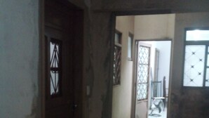 Un couloir faiblement éclairé, doté d’un sol carrelé, d’une porte en bois ornée d’un panneau de verre décoratif et d’une fenêtre avec une grille en métal.