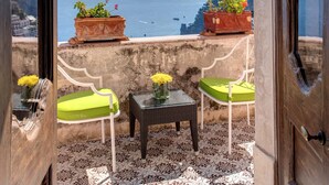 Un balcon avec vue sur la mer, deux chaises, une petite table et des plantes en pot.