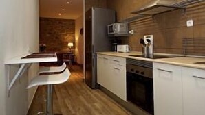 Une cuisine moderne avec des armoires blanches, une hotte de cuisinière en acier inoxydable et un four à micro-ondes. Le sol est en bois et il y a un petit coin repas avec une table et des chaises.