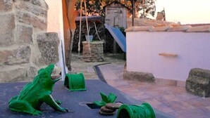 Une cour bordée de murs en pierre, ornée de sculptures vertes en forme de grenouille et comprenant un puits en pierre.