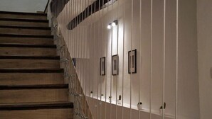 Un escalier en bois avec une rampe, menant à un palier où se trouve une étagère fixée au mur, sur laquelle sont disposées des photos encadrées et de petites plantes en pot.