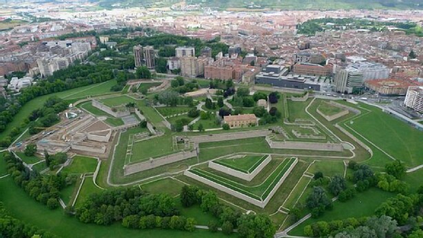 Vue aérienne d’un fort historique, entouré d’espaces verts, avec des bâtiments modernes en arrière-plan.