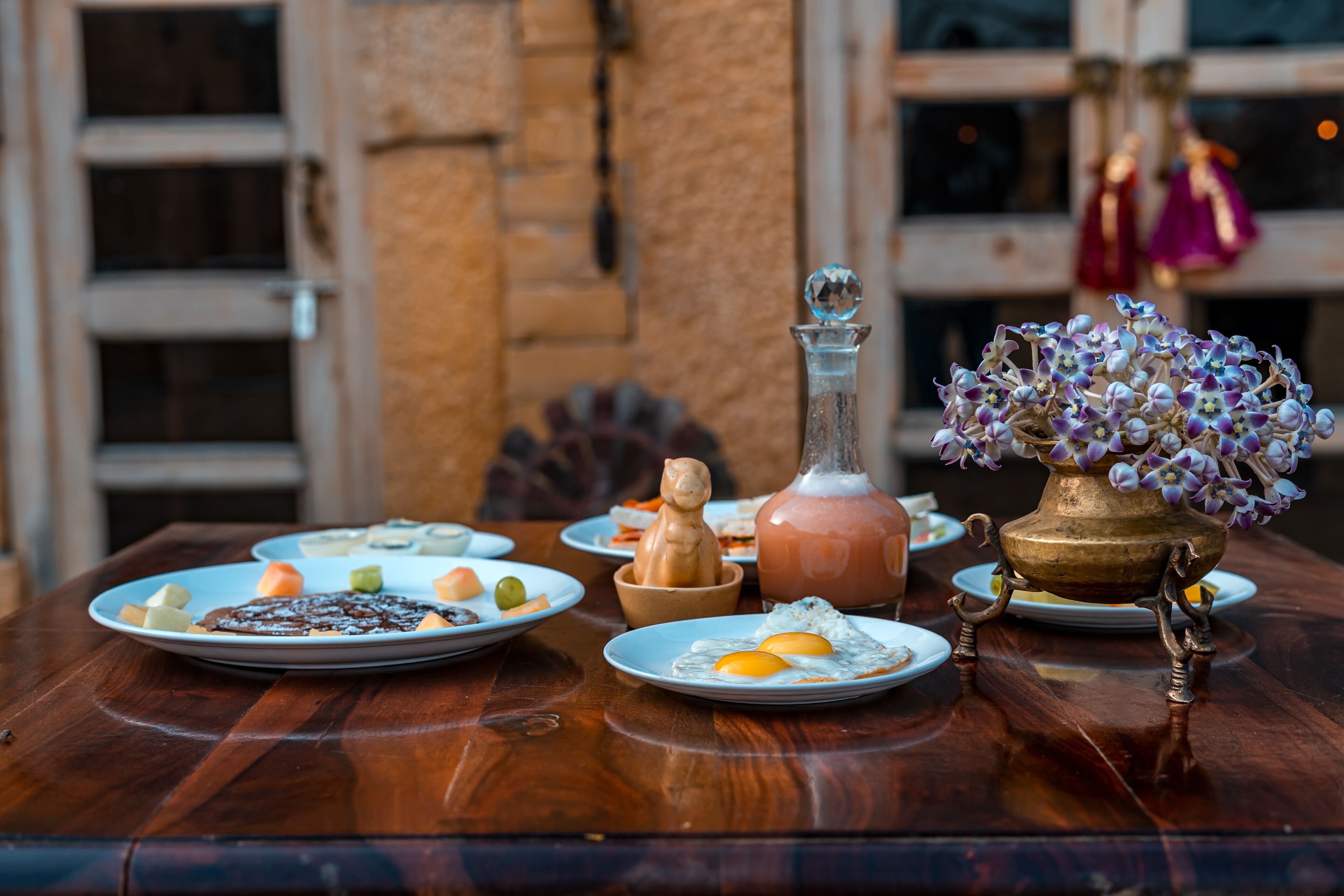 Une table en bois, sur laquelle on trouve des assiettes remplies de nourriture, une bouteille et un vase décoratif avec des fleurs.