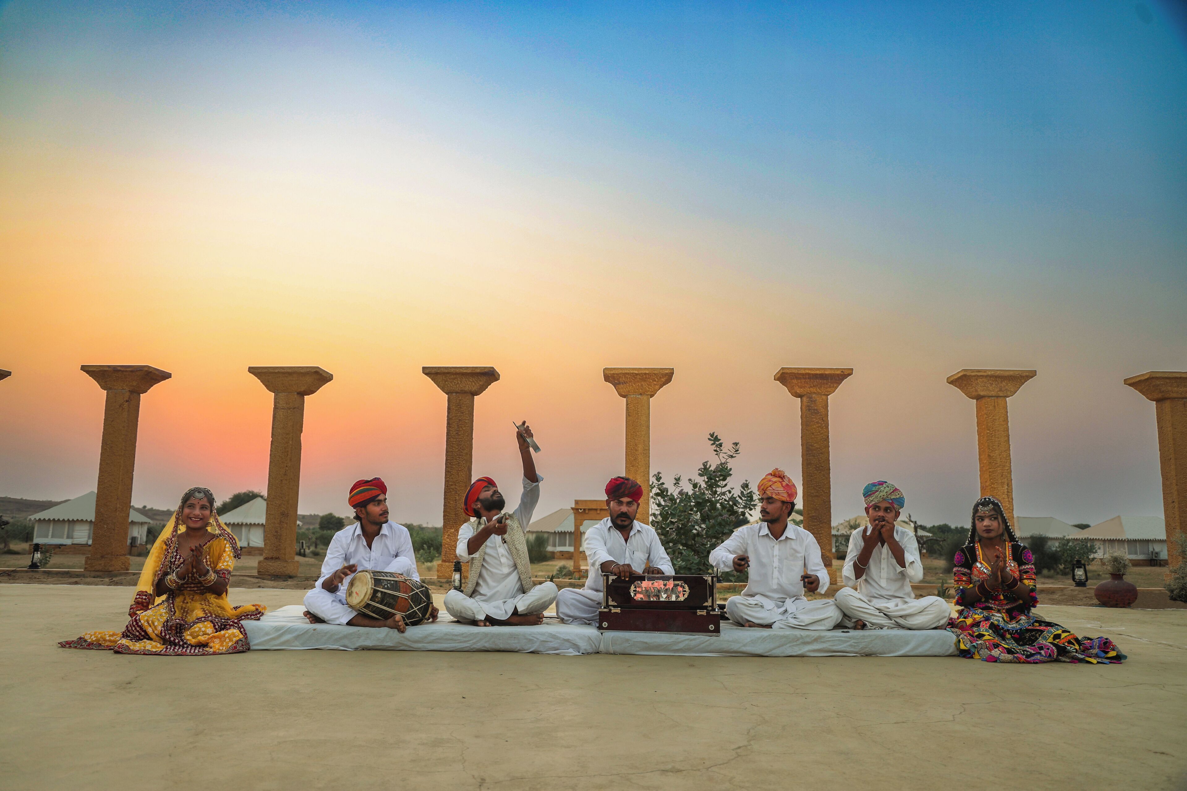 A group of people sitting on the ground in front of ancient columns during sunset.