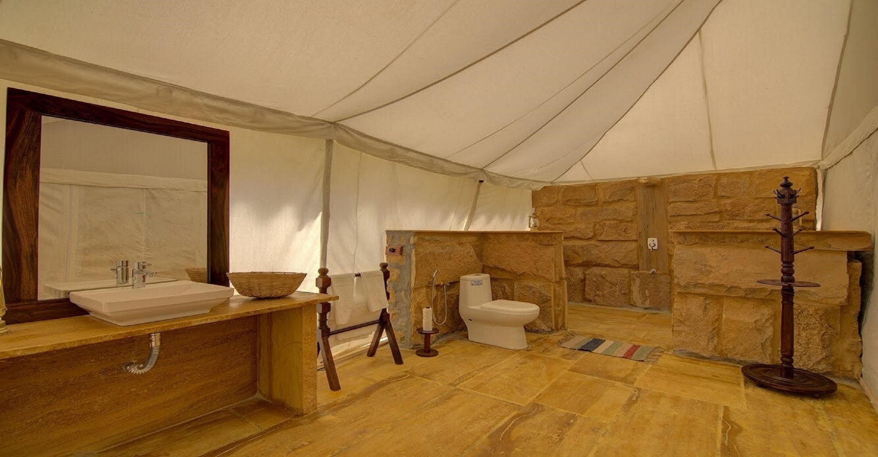 A tented bathroom with a stone wall, a sink, a toilet, and a mirror.
