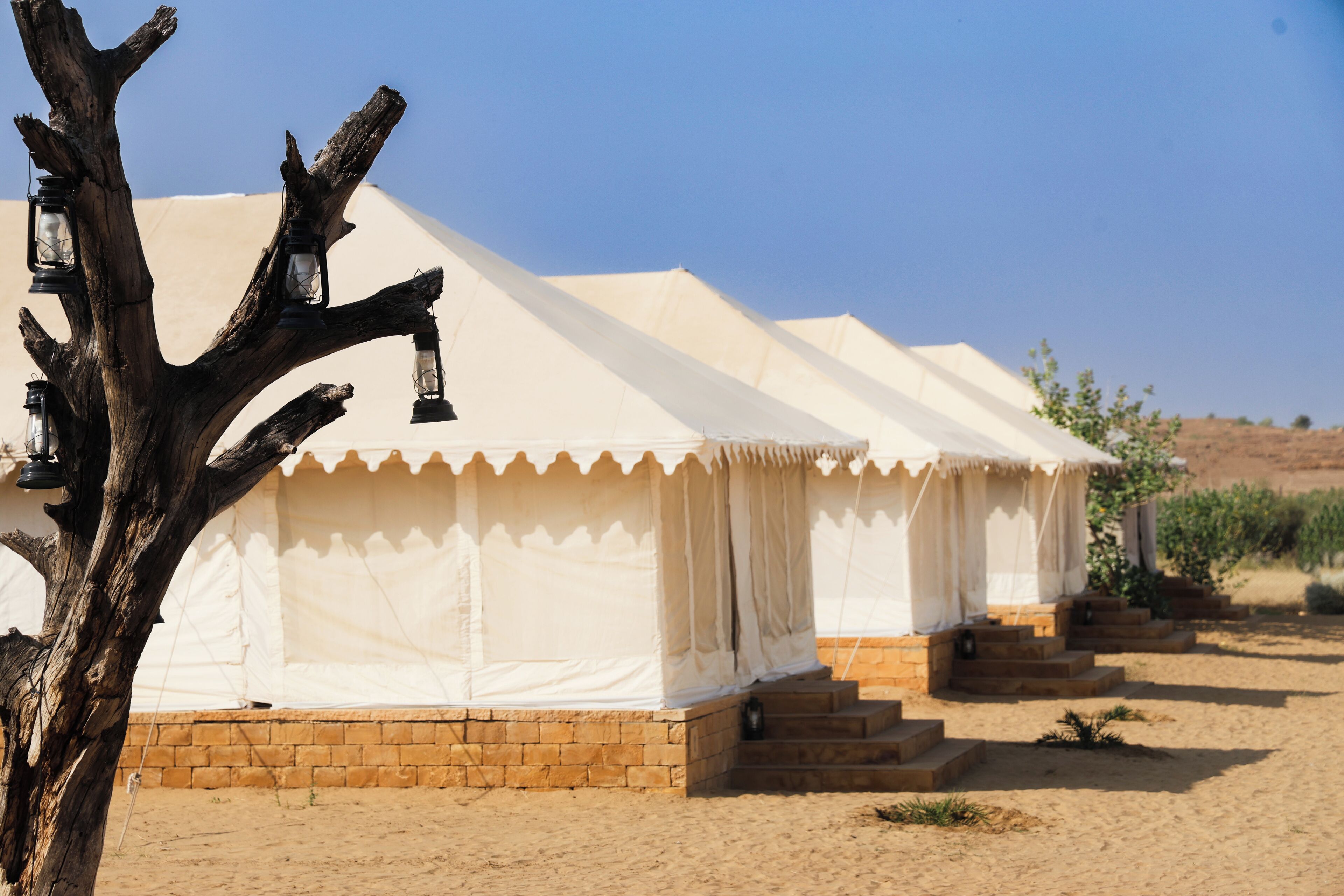 Een tent in de woestijn, met een fundering van bakstenen, trappen die erheen leiden, en lantaarns aan een boom.