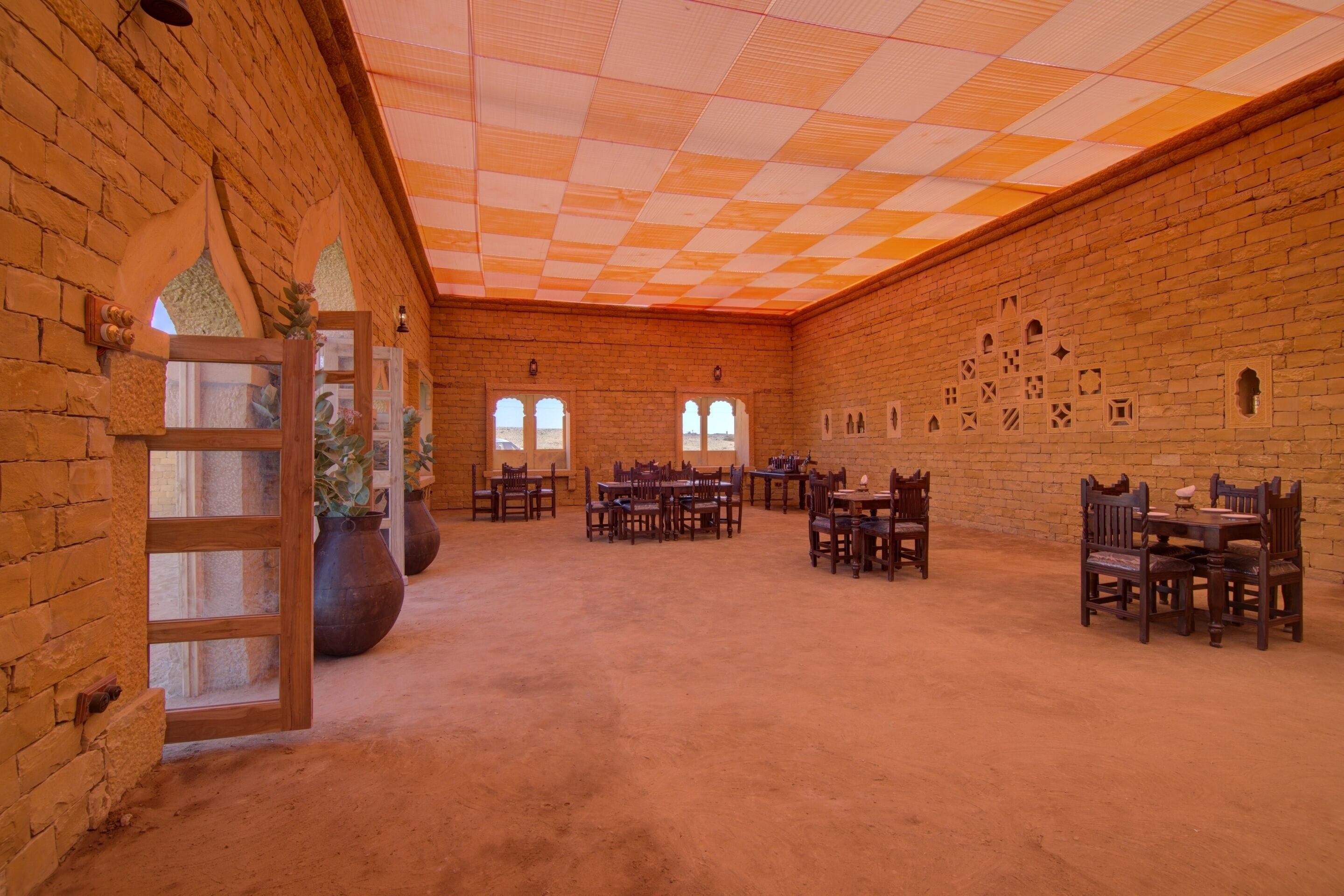 A spacious room with brick walls, wooden tables and chairs, and a checkered ceiling.